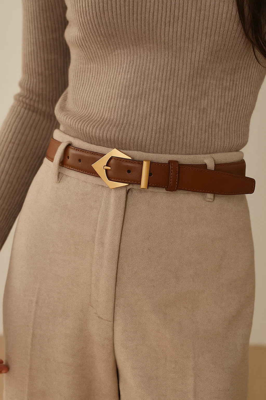 Person wearing a beige ribbed sweater and beige pants with a brown belt and gold buckle.