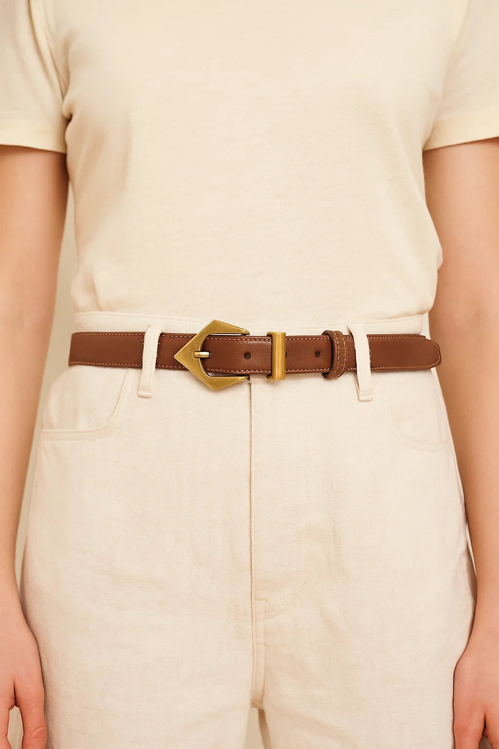 Person wearing a brown belt with a gold buckle on beige pants and shirt.